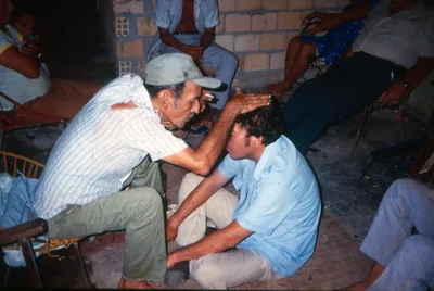 The curandero Solón Tello leaning over a seated man, his hand on the man’s head, in 1987.