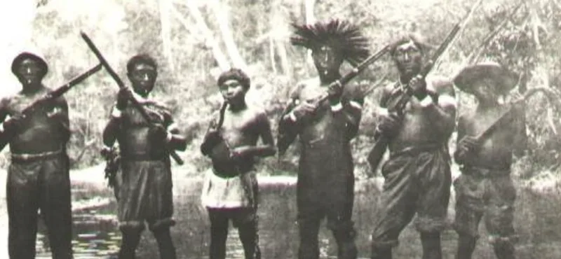 Six Kaxinawá men standing in a forest clearing on the upper Jordão River, several holding guns; an early twentieth-century photograph.