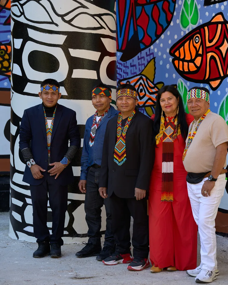 Five members of the MAHKU collective standing in front of a large painted wall of bold black-and-white patterns and coloured fish, at the 2024 Venice Biennale.