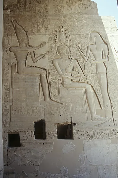 Temple relief: a king seated within the outline of a leafy tree, a crowned god seated at left with a raised writing hand, and a standing figure at right