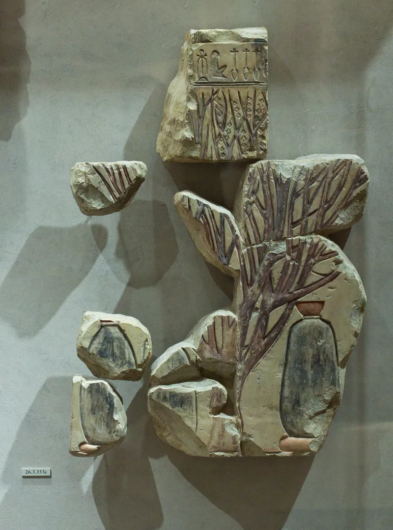 Fragments of a limestone relief: a tree with branching limbs incised and painted red, shading tall dark water jars with cups set on their mouths; a band of hieroglyphs above