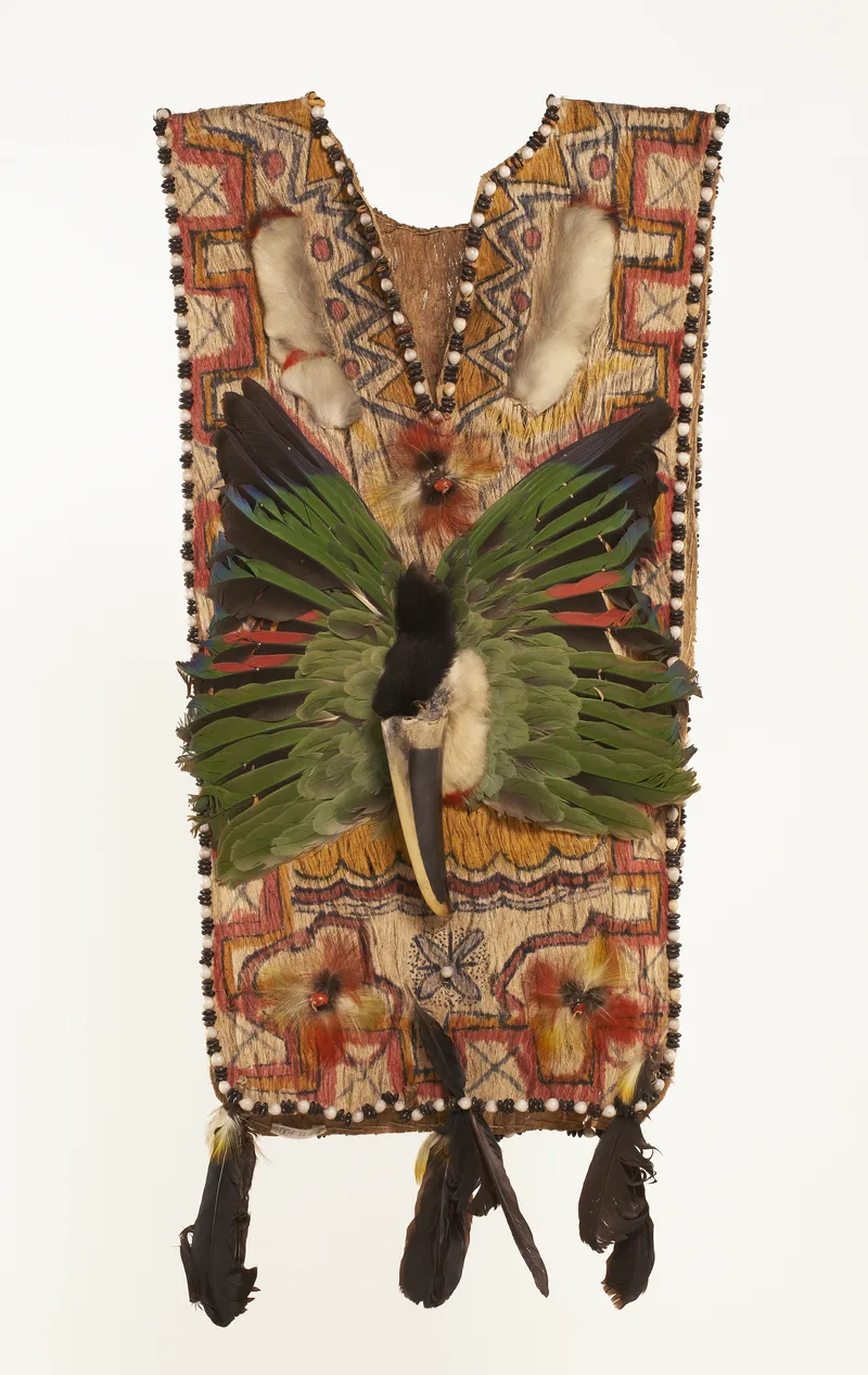 A Shuar shaman’s tunic of bark cloth painted with geometric designs in red, yellow and black, with green feathers, a toucan’s beak at the chest and black feathers hanging from the hem. Museum aan de Stroom, Antwerp.