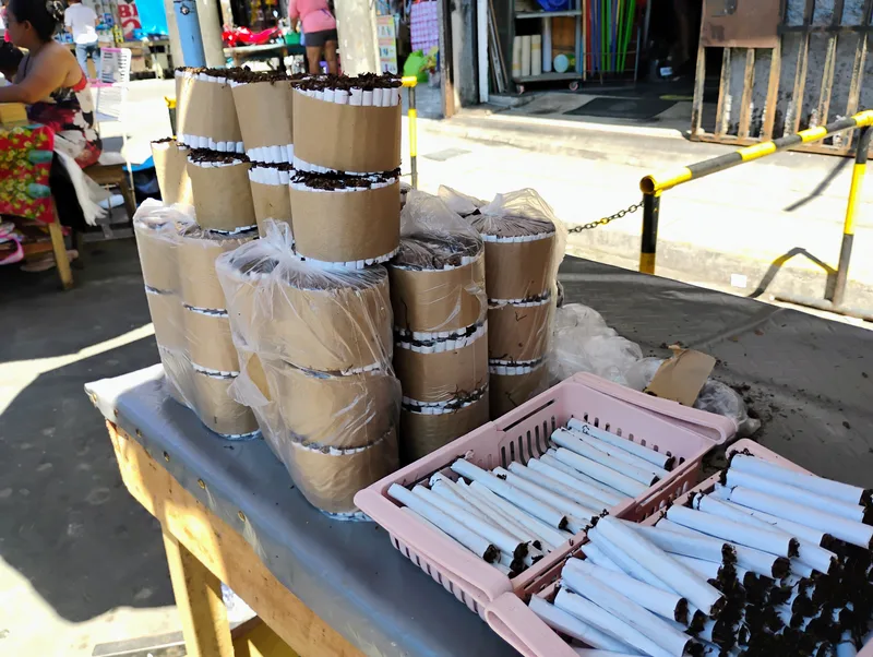 Hand-rolled mapacho cigarettes in pink baskets and paper-wrapped bundles of tobacco on a market stall, Belén market, Iquitos, 2024.