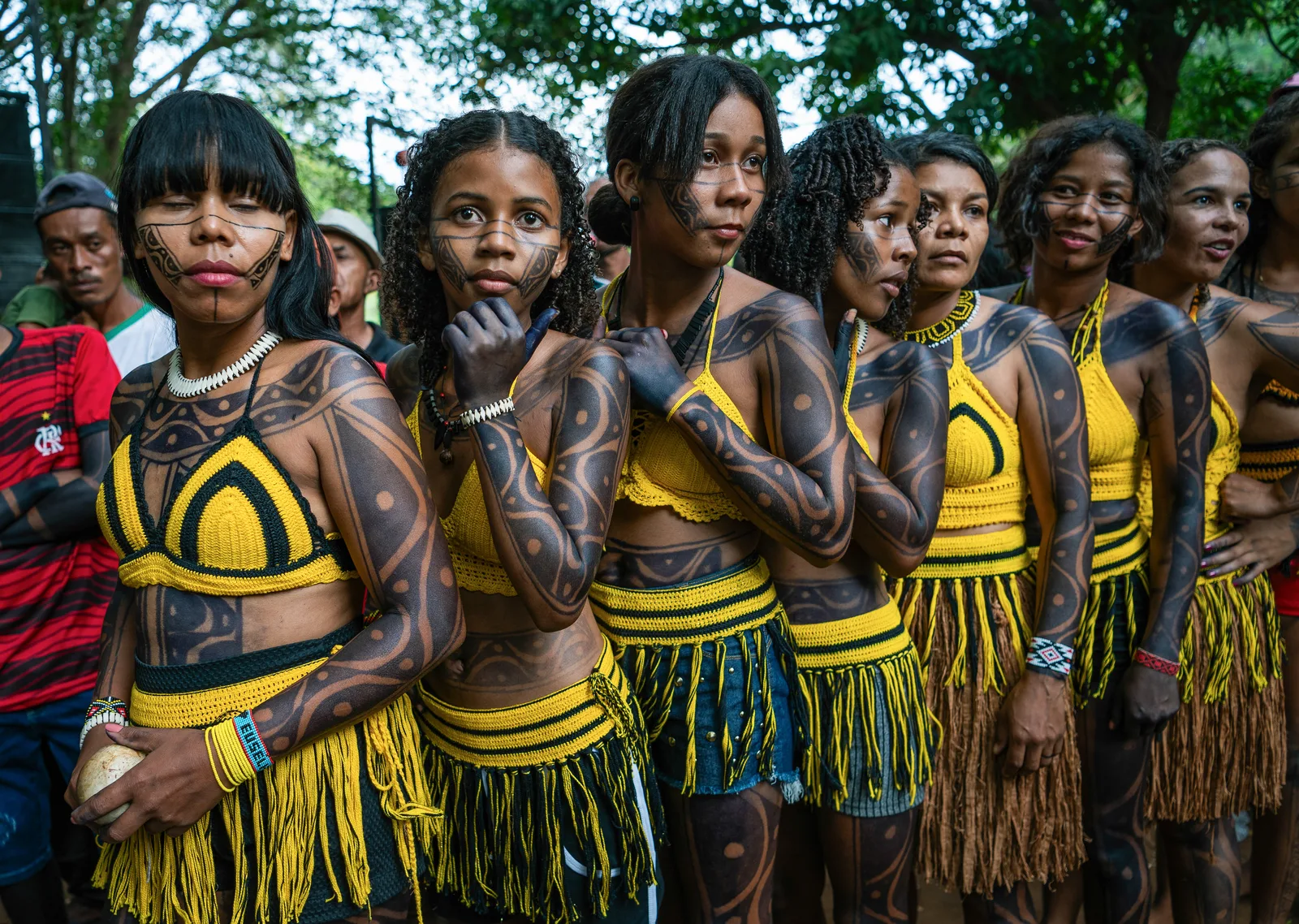Xakriabá women and girls in black body paint and woven yellow-and-black dress standing in a line at a toré